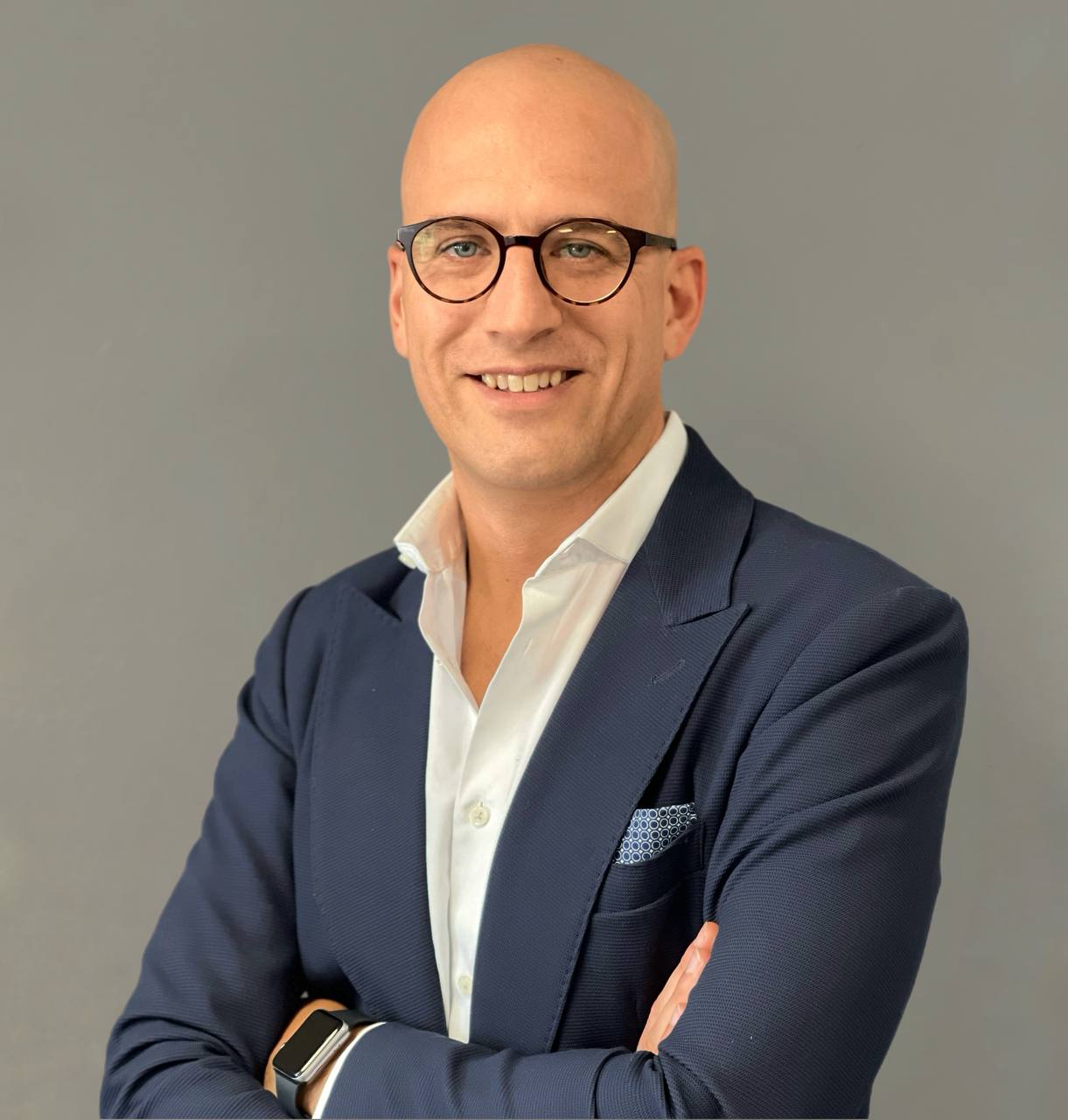 Foto di Carlo Apostoli a mezzo busto con braccia incrociate, camicia bianca, giacca blu su sfondo grigio